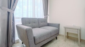 A room with a grey sofa, a small wooden table, and a window with curtains. - Warm and Cozy Studio Room at Menteng Park Apartment (Jakarta)