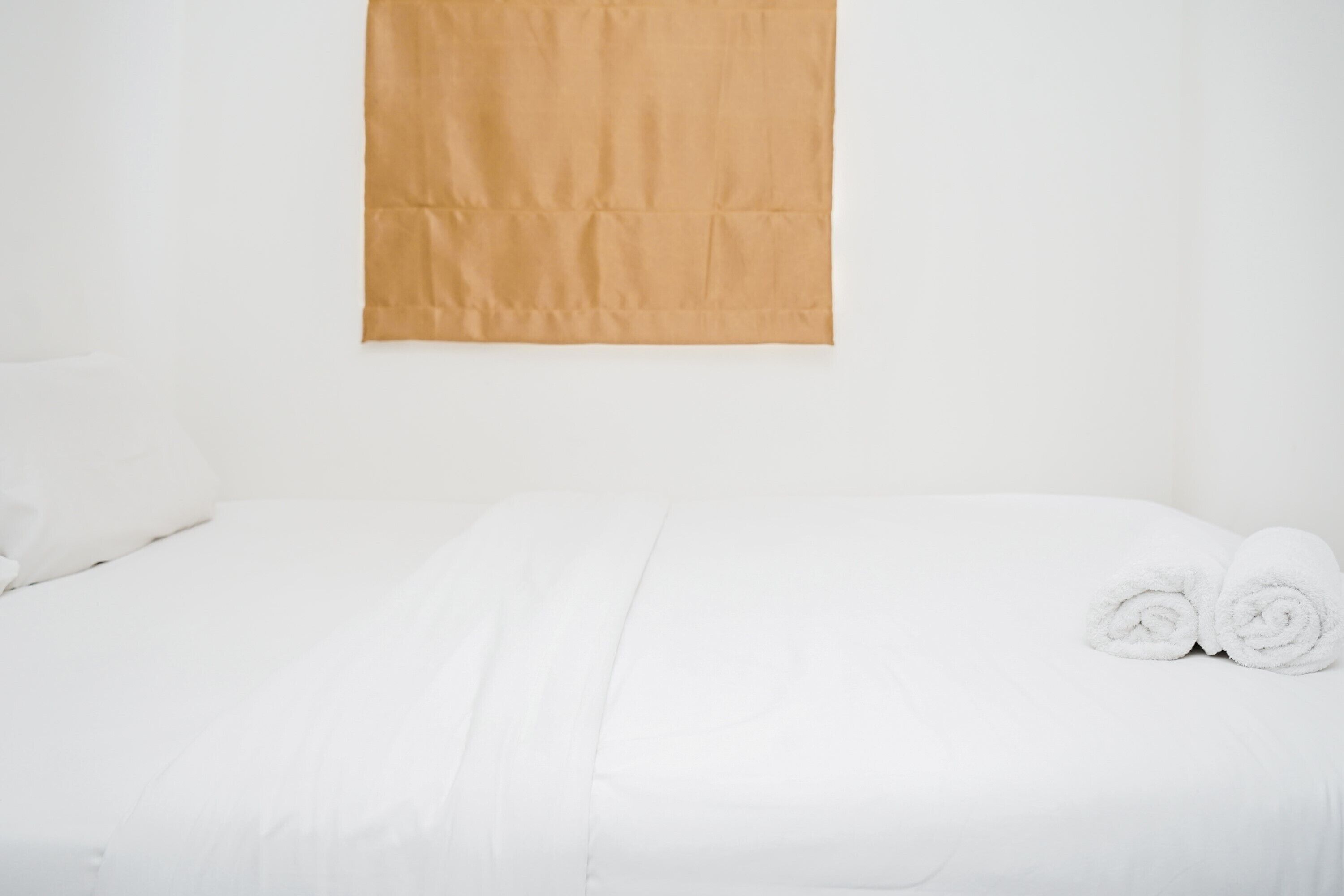A neatly made bed with white bedding and two rolled towels on the side.