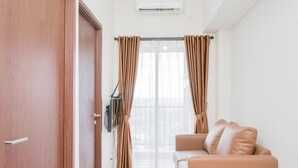 A room with a wooden door, a television mounted on the wall, a window with curtains, and a beige sofa. - Comfy 2BR Apartment at Parkland Avenue (South Tangerang)