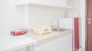 A kitchen with white cabinets, a sink, a red portable heater, and a white refrigerator. - Comfy 2BR Apartment at Parkland Avenue (South Tangerang)