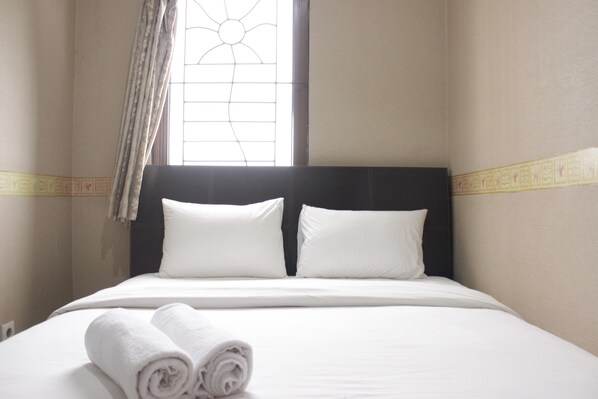 A hotel room with a neatly made bed, two pillows, and rolled towels on the bed.
