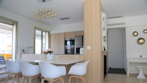 A modern kitchen with a central island, white chairs, and a hanging light fixture. - Rooftop Croisette/alexandre III (CANNES)
