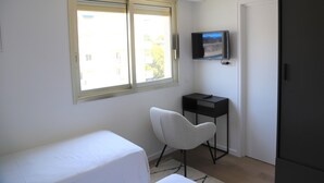 A small, sparsely furnished room with a bed, a chair, a desk with a TV, and a wardrobe. - Rooftop Croisette/alexandre III (CANNES)