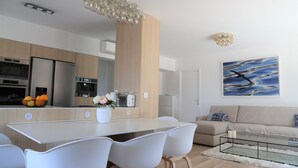 A modern kitchen with a central island, white chairs, a dining table, and a living area with a sofa and a painting. - Rooftop Croisette/alexandre III (CANNES)