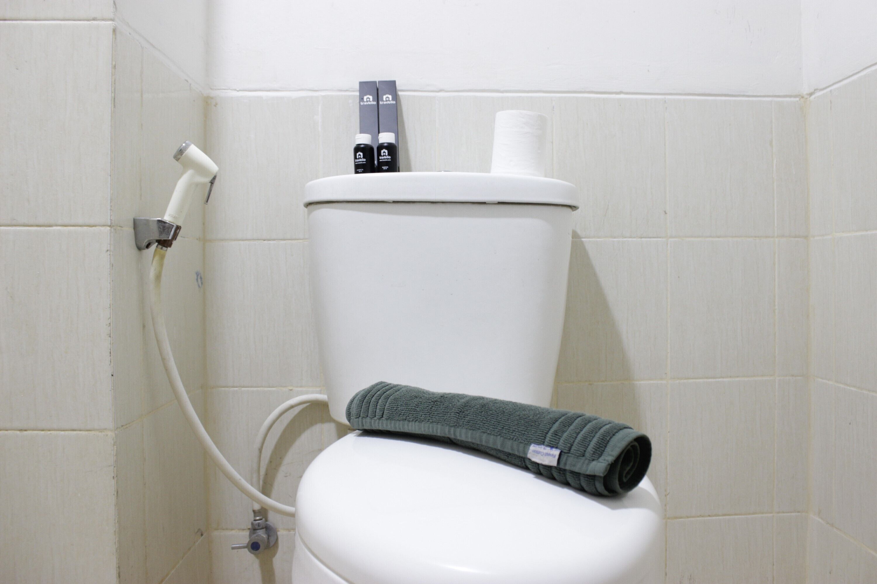 A white toilet with a green towel, a toilet paper holder, and a bidet attachment.