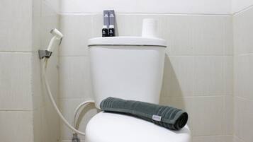 A white toilet with a green towel, a toilet paper holder, and a bidet attachment.