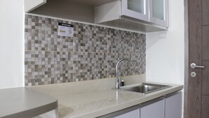 A kitchen with a tiled backsplash, a stainless steel sink, and white cabinets.