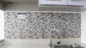 A kitchen with a tiled backsplash, a stainless steel sink, and a caution sign.