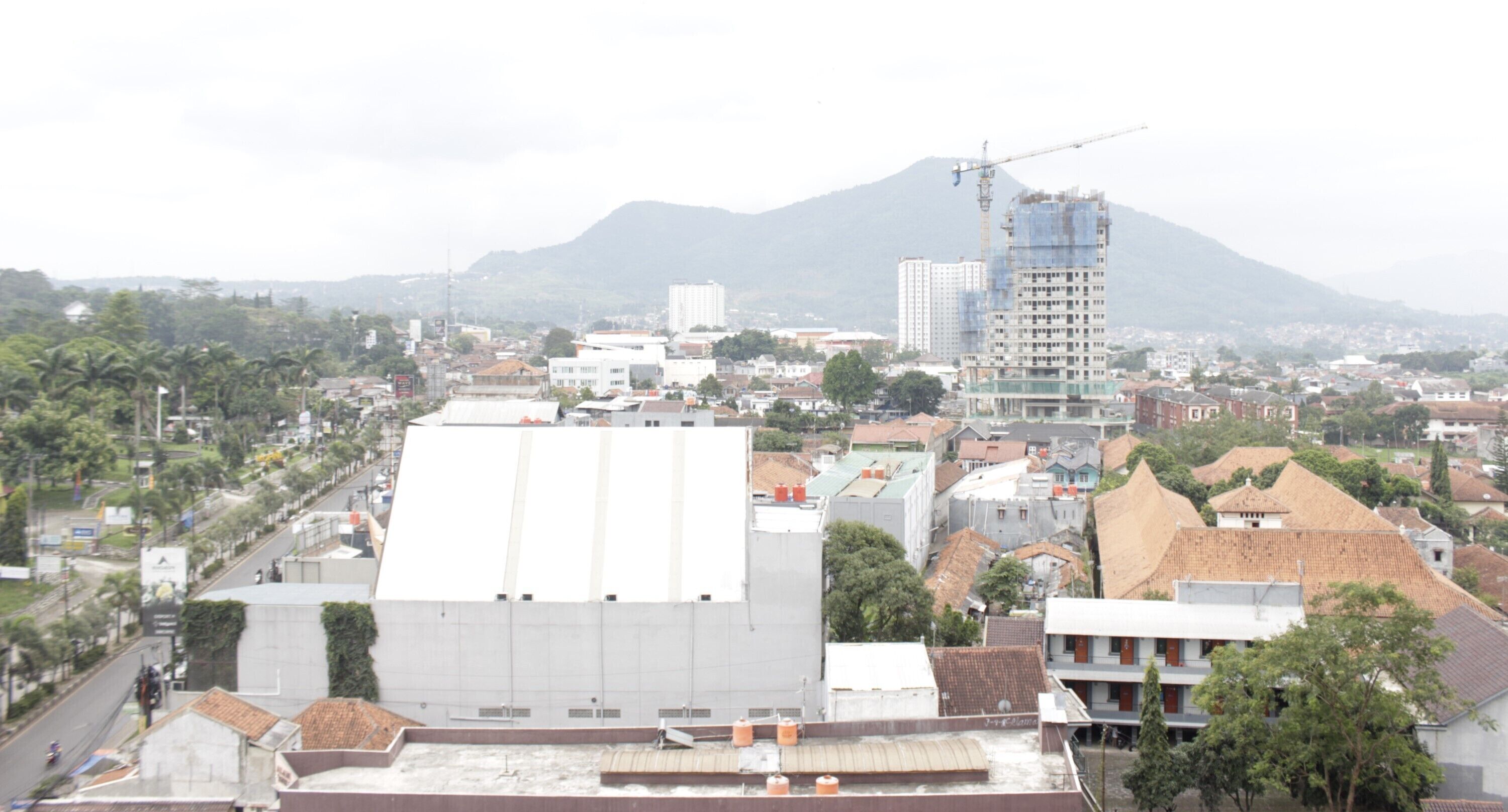 A cityscape with a prominent white building in the foreground, a construction site with a crane, and a mountain in the background.