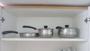 A kitchen with three stainless steel pots on a white shelf.