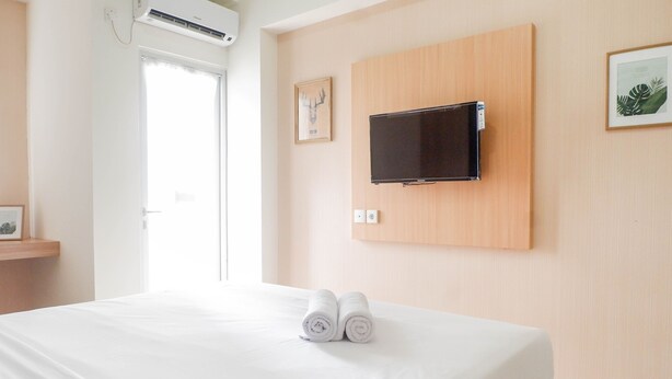 A hotel room with a bed, a mounted TV, and two rolled towels on the bed.