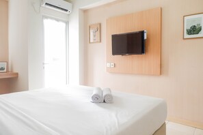A hotel room with a bed, a mounted TV, and two rolled towels on the bed. - Best Value & Clean Studio Room Apartment at Pavilion Permata 2 (Surabaya)