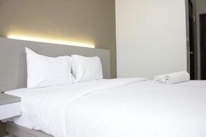 A neatly made bed with white linens and pillows, a bedside table, and a rolled towel.