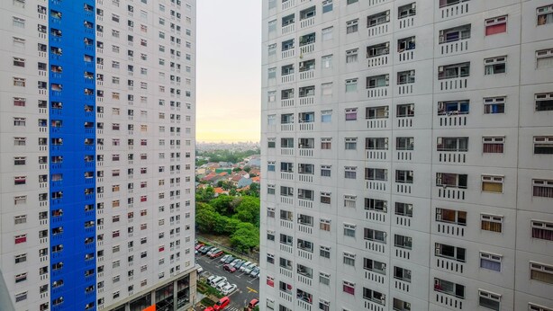 A high-rise building with multiple floors, a blue vertical stripe on the left, and a view of a parking area below.