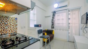 A compact kitchen with a gas stove, a small dining area with a chair, and a TV mounted on the wall.