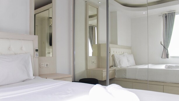 A modern hotel room with a large bed, a bedside table, a mirror, and a wardrobe. - Comfort 2BR Bassura City Apartment near Shopping Center (Jakarta)