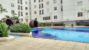 A swimming pool surrounded by potted plants and a multi-story building with balconies. - Comfort 2BR Bassura City Apartment near Shopping Center (Jakarta)