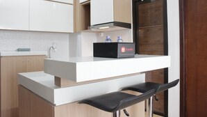 A modern kitchen with white cabinetry, a black countertop, and a bar stool. - Deluxe & Cozy 3BR at Gateway Pasteur Apartment (Cimahi)