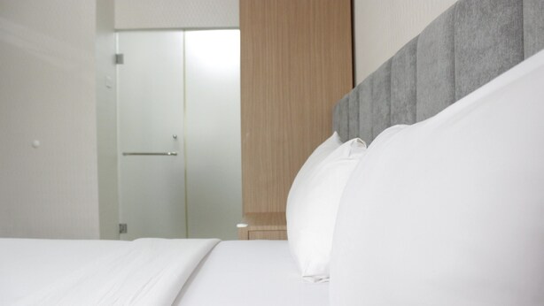 A modern hotel room with a large bed, a wooden wardrobe, and a glass door leading to a bathroom. - Deluxe & Cozy 3BR at Gateway Pasteur Apartment (Cimahi)