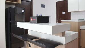 A modern kitchen with a black refrigerator, a white countertop, and two black bar stools. - Deluxe & Cozy 3BR at Gateway Pasteur Apartment (Cimahi)