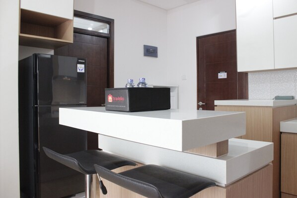 A modern kitchen with a black refrigerator, a white countertop, and two black bar stools.