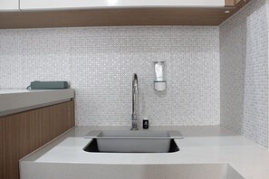 A modern kitchen with a white countertop, a stainless steel sink, and a tiled backsplash. - Deluxe & Cozy 3BR at Gateway Pasteur Apartment (Cimahi)