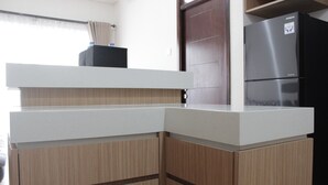 A kitchen with a white countertop, wooden cabinets, and a black refrigerator. - Deluxe & Cozy 3BR at Gateway Pasteur Apartment (Cimahi)