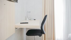 Une petite pièce moderne, équipée d’un bureau, d’une chaise et d’une fenêtre avec des rideaux.