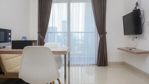 Ein modernes Hotelzimmer mit großem Fenster, Schreibtisch mit Computer, Stuhl und einem an der Wand montierten Fernseher.