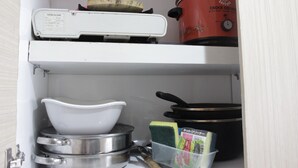 Une cuisine équipée d’une cuisinière à gaz mobile, d’une mijoteuse électrique rouge, d’un saladier blanc, d’une poêle et d’un récipient en plastique contenant des produits de nettoyage.