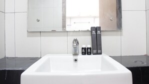 Un lavabo dans une salle de bain, avec un miroir au-dessus. On y trouve trois brosses à dents et une bouteille de bain de bouche.