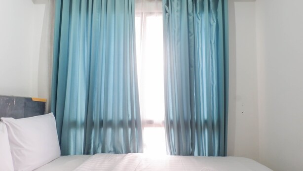 Une chambre d’hôtel avec un lit, du linge de lit blanc et des rideaux bleus.