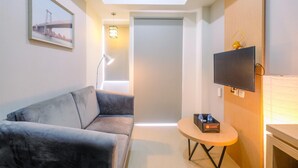 Un hotel moderno con un sofá gris, una mesita redonda con una botella, un televisor de pantalla plana y un cuadro en la pared.