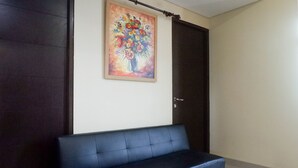 Une pièce avec un canapé de couleur sombre, un tableau représentant une composition florale accroché au mur et une porte sombre.