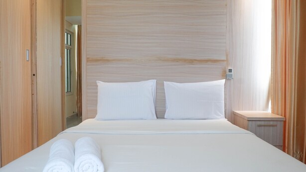 Un lit bien fait, avec du linge de lit blanc et deux oreillers, une tête de lit en bois, une table de chevet avec une lampe et une armoire en bois.