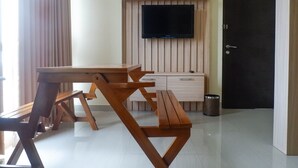 Une pièce avec une table et des bancs en bois, un téléviseur fixé à un mur en bois, une armoire blanche et une porte.