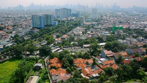 An aerial view of a cityscape with residential buildings, a large commercial building, and a distant skyline. - Comfort Studio at Green Pramuka Apartment near Shopping Center (Jakarta)