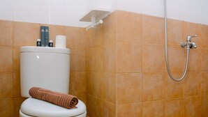 A bathroom with a toilet, a towel, and a shower head. - Comfort Studio at Green Pramuka Apartment near Shopping Center (Jakarta)