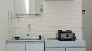 A kitchen with a sink, a mirror, a toaster, and a white brick wall. - Comfort Studio at Green Pramuka Apartment near Shopping Center (Jakarta)