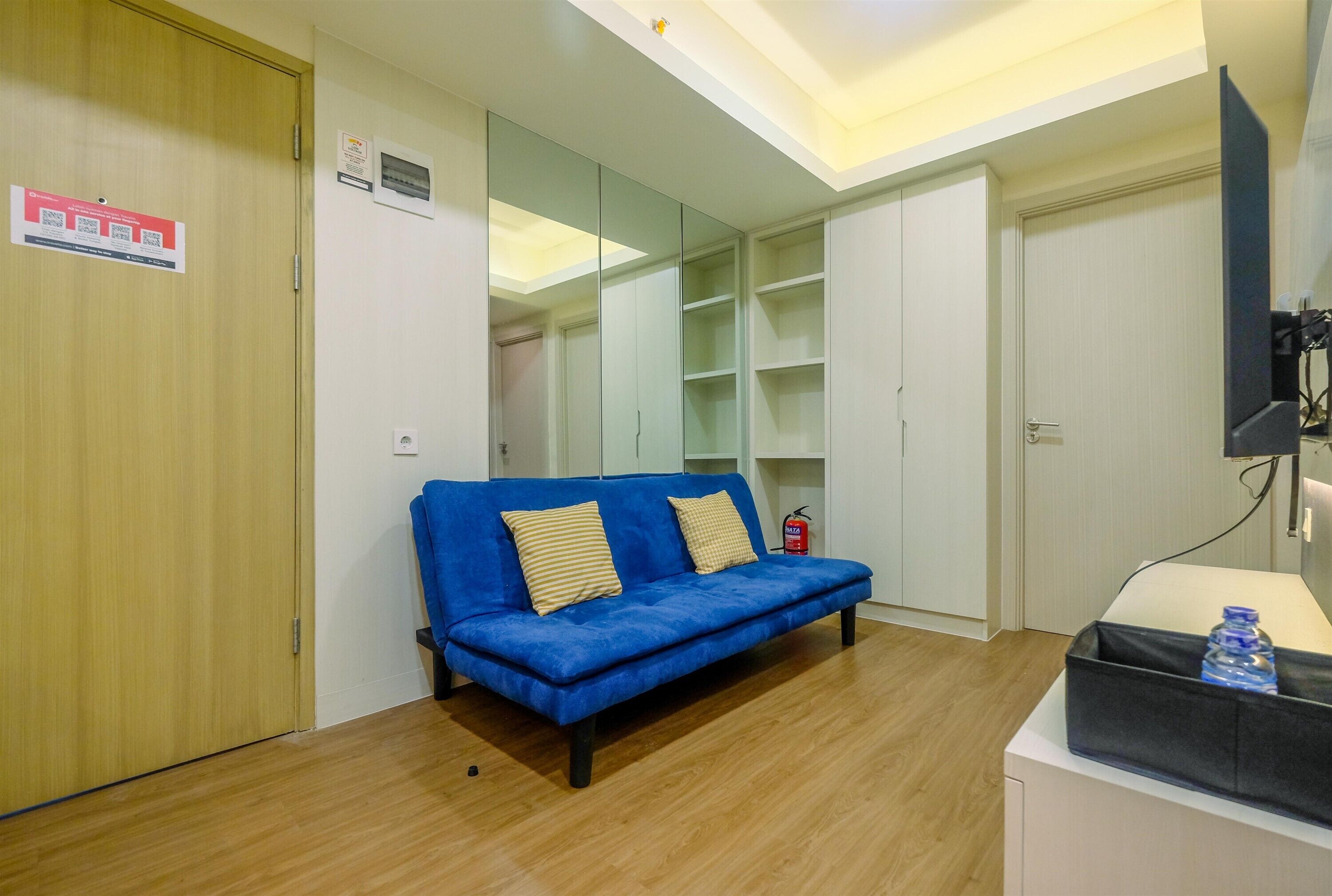Een kamer met een blauwe bank, een houten garderobe en een televisie op een standaard.