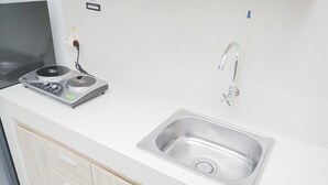 A kitchen with a stainless steel sink, a built-in stove, and wooden cabinets. - Comfort and Minimalist Studio Apartment at Springwood Residence (Tangerang)