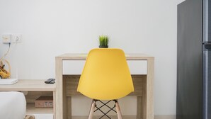 A modern kitchen with a yellow chair, a small plant on the chair, a wooden table, and a black refrigerator. - Comfort and Minimalist Studio Apartment at Springwood Residence (Tangerang)