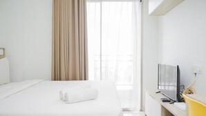 A hotel room with a bed, a TV, and a window with curtains. - Comfort and Minimalist Studio Apartment at Springwood Residence (Tangerang)