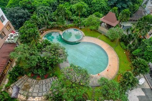 An aerial view of a resort with a large, circular swimming pool surrounded by lush greenery and a small building with a red roof. - Comfort 2BR Apartment at Cervino Village (Jakarta)