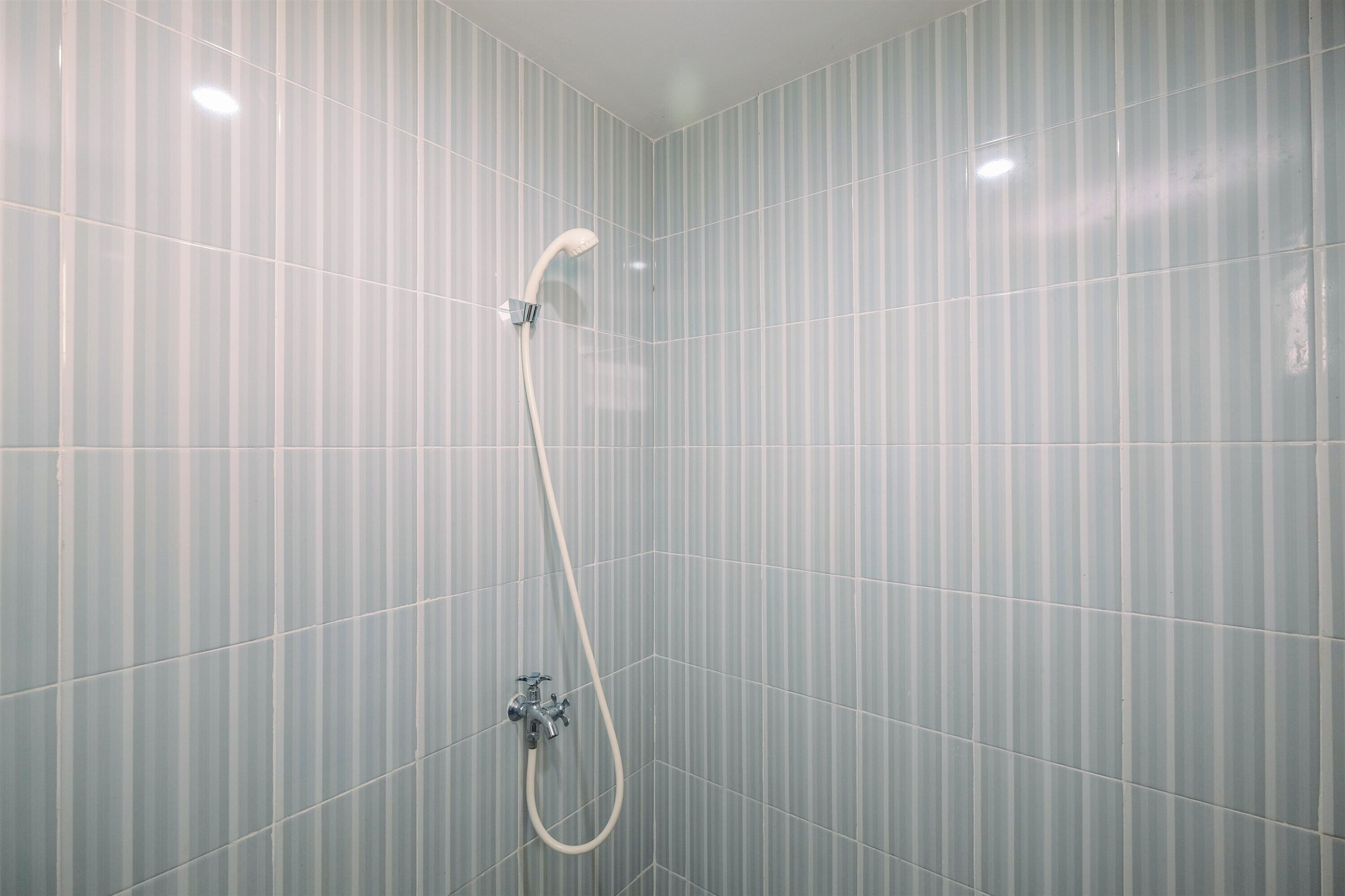 Chuveiro com chuveiro manual e torneira fixada na parede, em um ambiente com paredes de azulejos listrados.