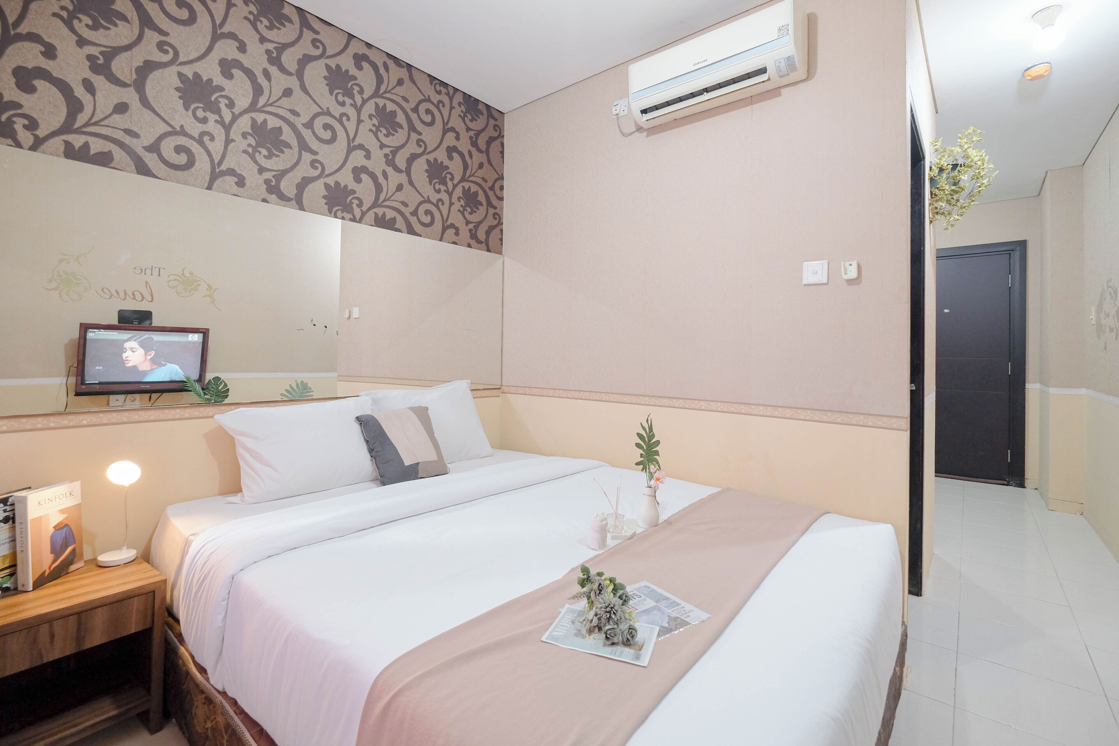 A hotel room with a bed, bedside table, lamp, air conditioning unit, and a wall with a decorative pattern.