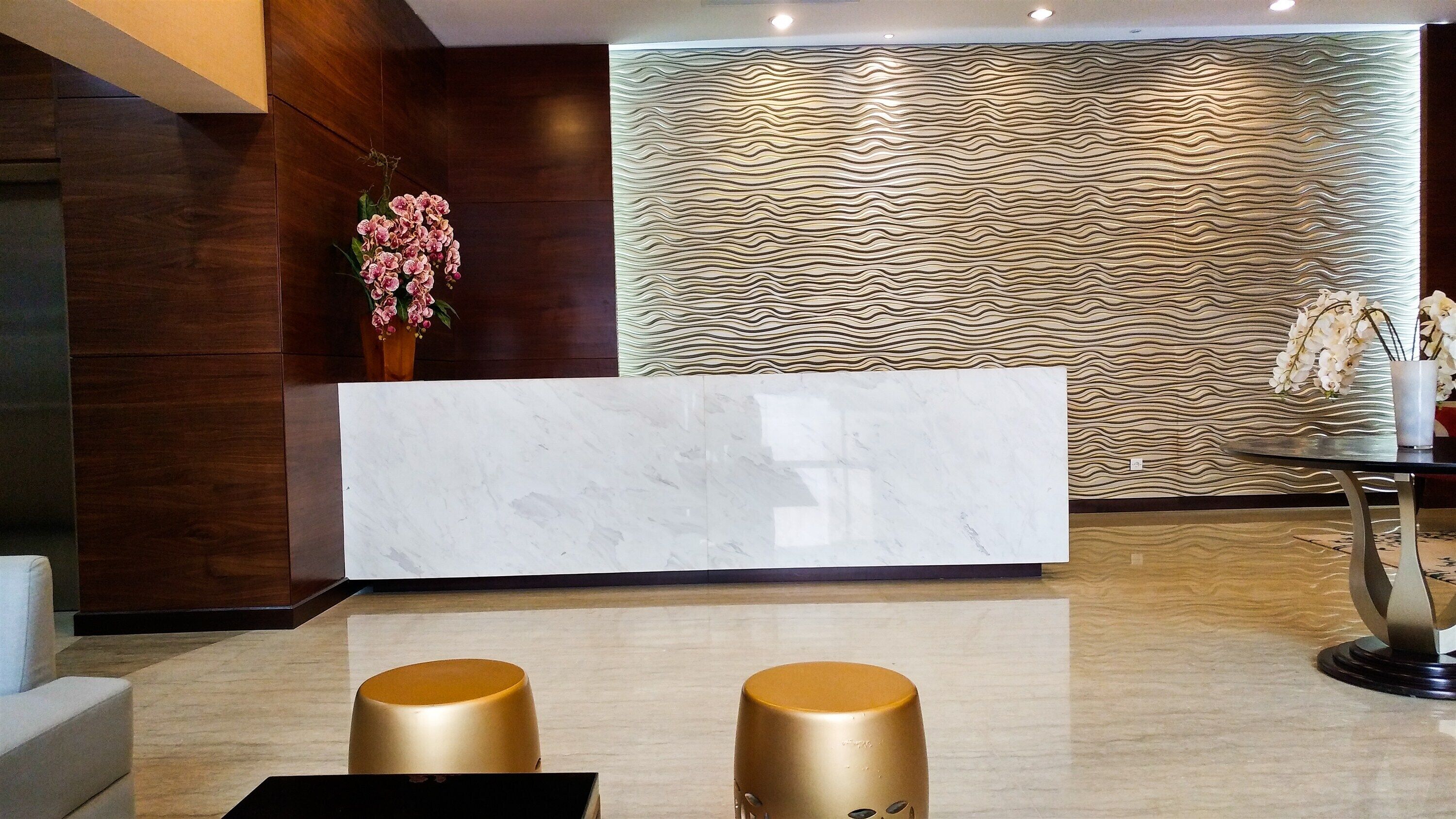 A reception area with a marble counter, wooden panel wall, and two gold stools.