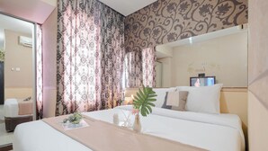 A hotel room with a large bed, a bedside table, a mirror, and a decorative plant.