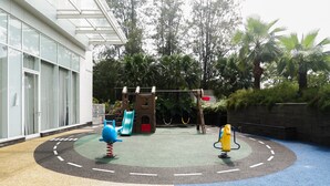 A children's play area with a slide, climbing structure, and swings. - Spacious Studio Room Apartment at Grand Sungkono Lagoon (Surabaya)