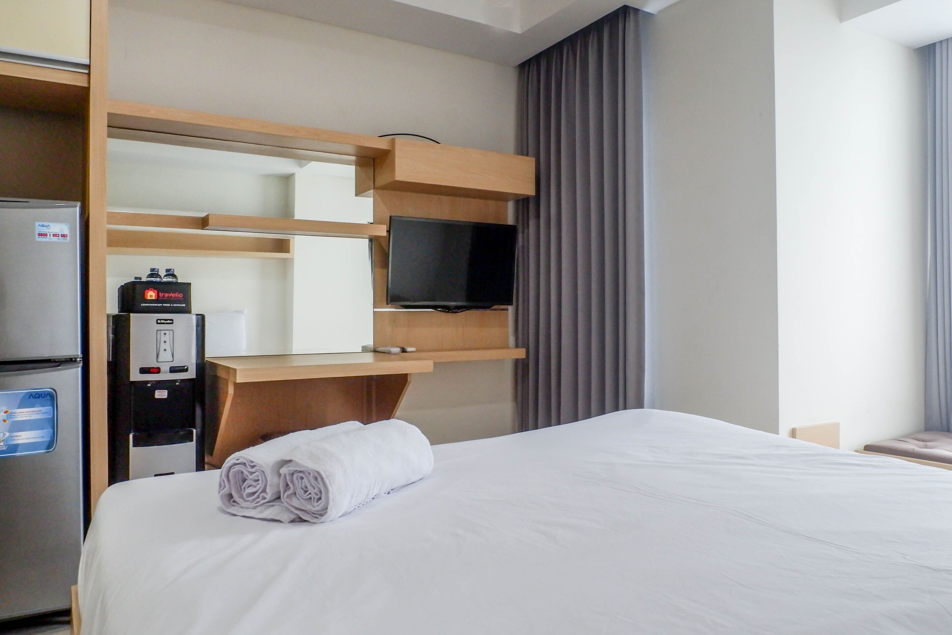 Una habitación de hotel con cama, televisor, minibar y refrigerador.